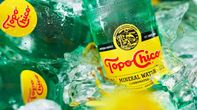 Close-up of a Topo Chico bottle label surrounded by crushed ice and yellow citrus.
