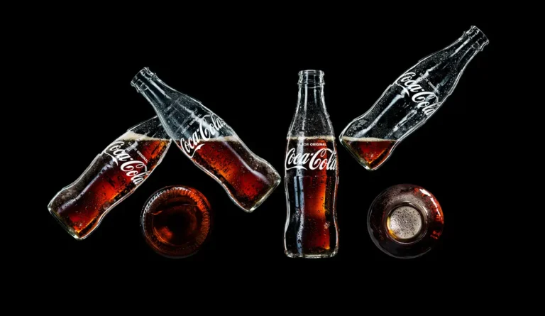 Two Coca-Cola glass bottles clinking together against a dark, moody background.
