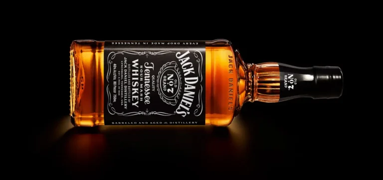 A bottle of Jack Daniel’s Tennessee Whiskey lying horizontally against a black background.