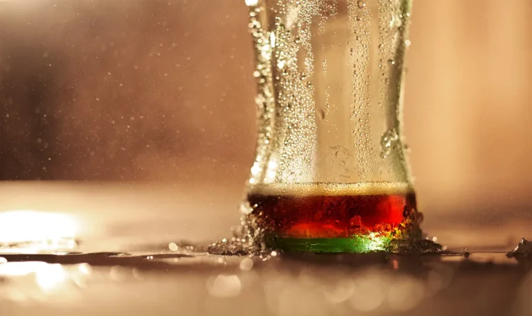 A glass filled with dark soda and ice, showing condensation on the outside.