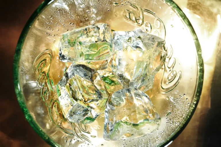 Top-down view of a glass filled with ice and clear soda, showing bubbles and light refraction.