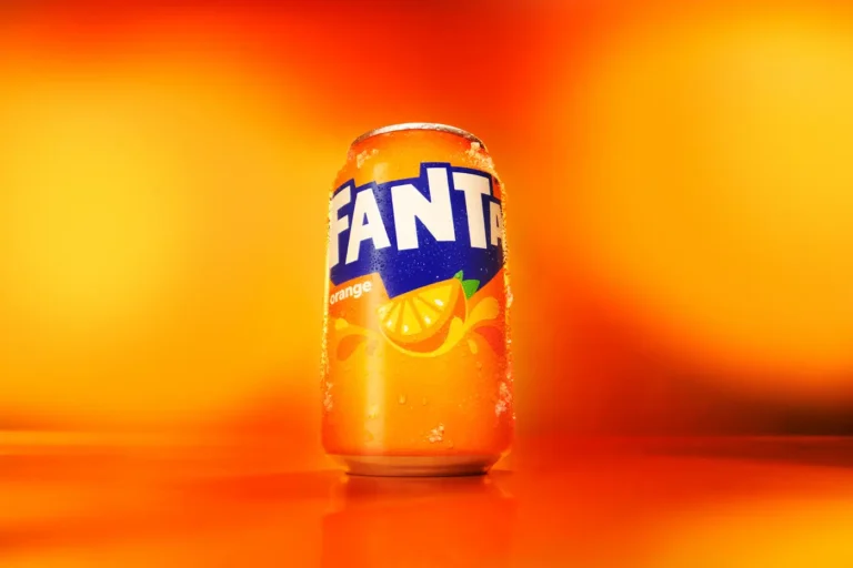 Close-up of a glass being filled with sparkling orange soda against a bright orange background.