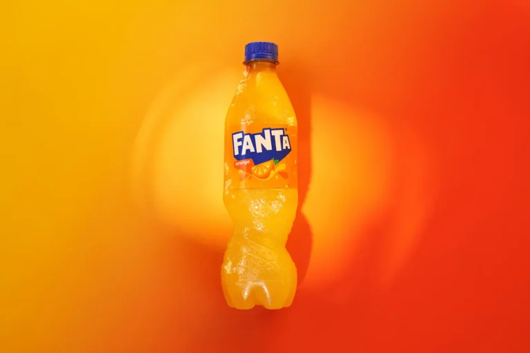 An orange Fanta bottle centered against a vibrant orange background with a slight shadow.
