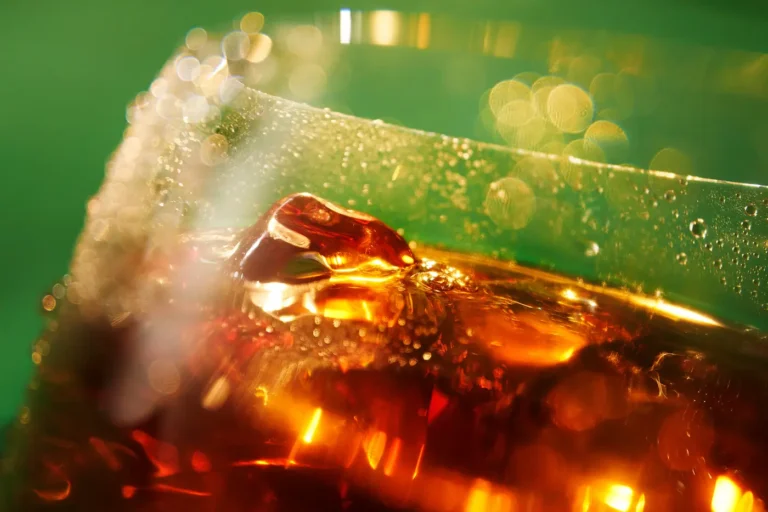 Close-up of amber liquid and ice cubes inside a glass with condensation.