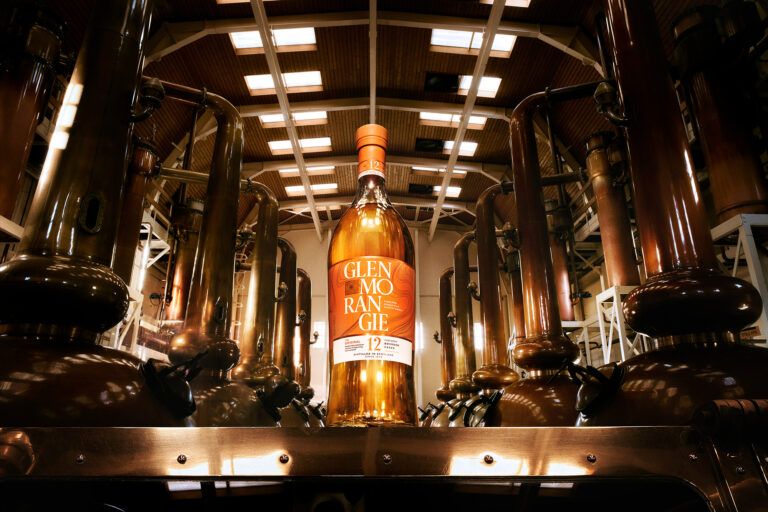 A bottle of Glenmorangie whiskey standing inside a dark, modern wooden cellar.